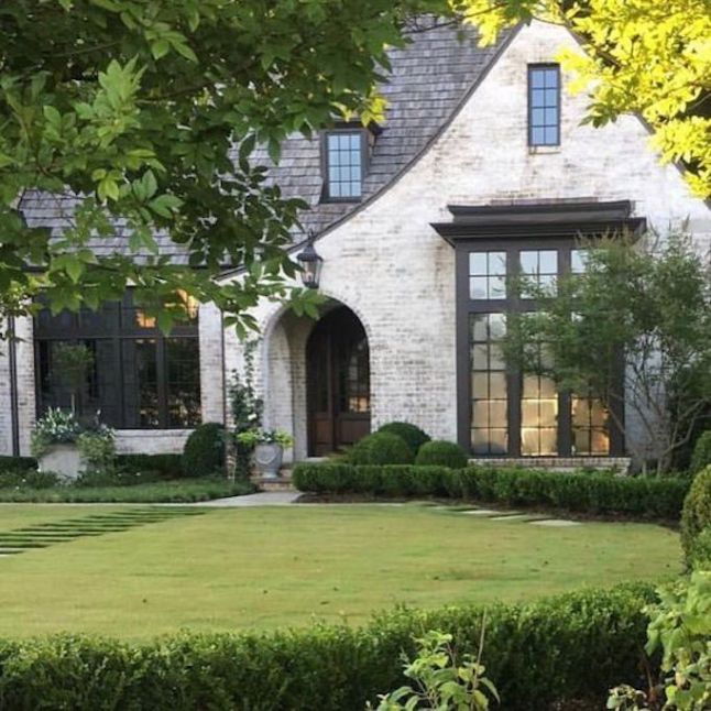 Exterior of a home that looks like German schmear facade with lots or shrubs and brushes around the home